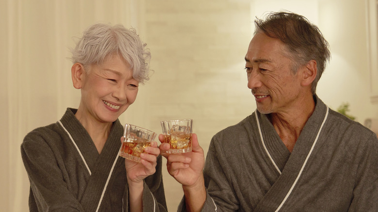 Äldre par skålar med whiskey sängfösare i hotellrum