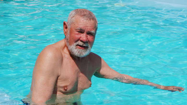 Senior man med solbränd hud som ler medan han står i en pool