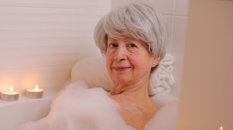 Senior kvinna som tar ett bad med ljus och skum runt omkring henne