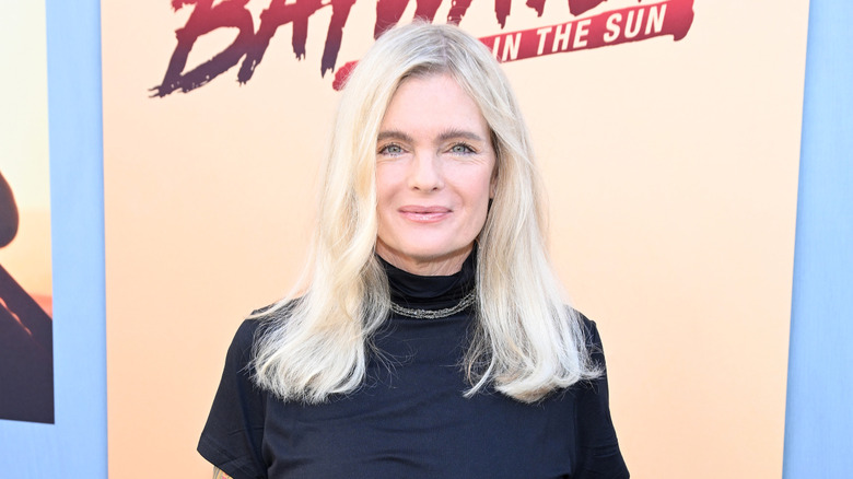 Erika Eleniak vid ett evenemang 2024 klädd i en svart mock turtleneck-topp med ett enkelt halsband.