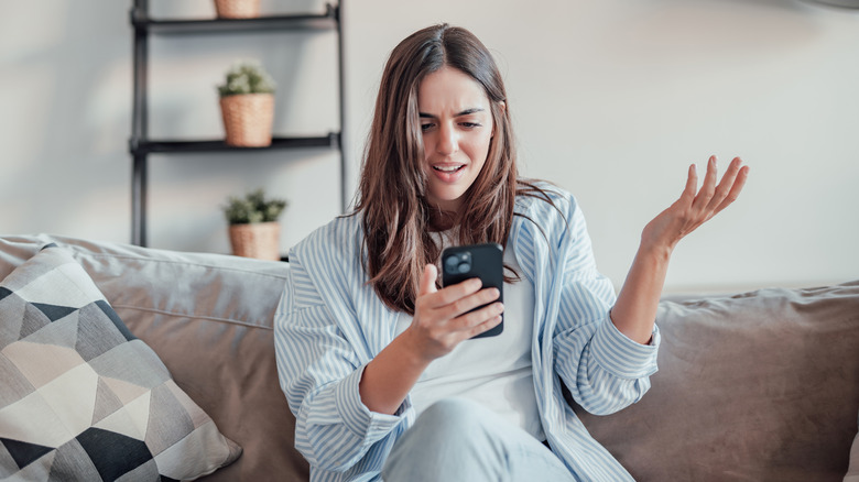 En kvinna tittar irriterat på sin telefon