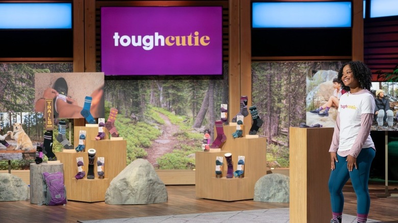 ToughCutie-grundaren Brittany Coleman bär en vit t-shirt med sin företagslogotyp över en långärmad rosa huvtröja med jeans och sina ToughCutie-strumpor medan hon ställer upp på Shark Tank, som sänds i januari 2025.