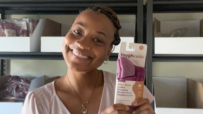 ToughCutie-grundaren Brittany Coleman bär upp håret tillsammans med en ljusrosa t-shirt och små ringörhängen medan hon visar upp en ny färg på strumpor i juli 2025.