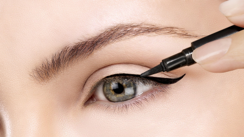 Närbild av en person som applicerar en svart eyelinervinge med ögat öppet