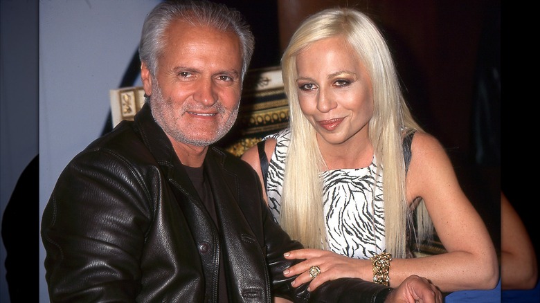 Gianni Versace i en svart skinnjacka som sitter bredvid syster Donatella klädd i en svart-vit topp cirka 1996.