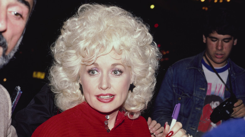 Dolly Parton skriver autografer 1984 klädd i en röd topp med stjärnformade örhängen.