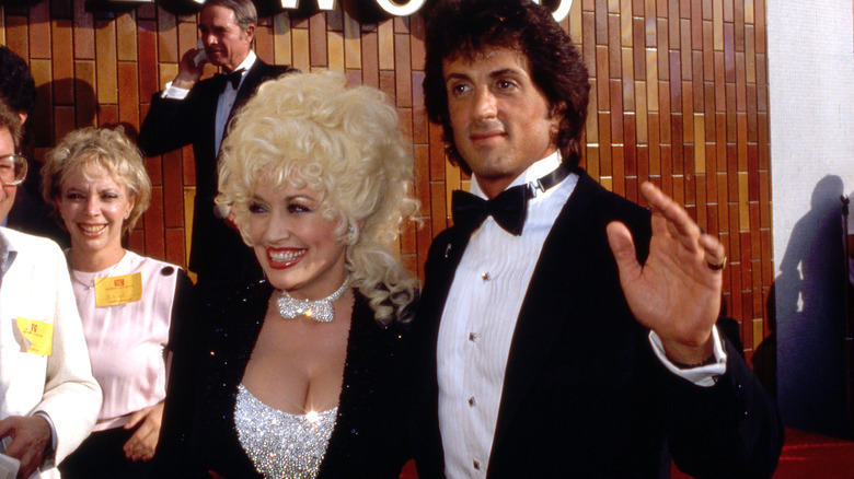 Dolly Parton 1984 poserar med Sylvester Stallone klädd i en glittrande silvertopp med matchande fluga och en svart glittrig jacka.