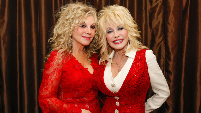 Stella Parton och Dolly Parton poserar tillsammans i matchande glittrande röda outfits.