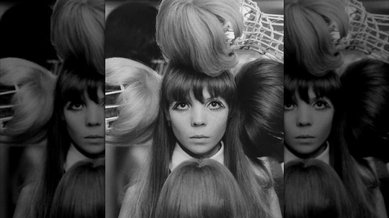 Modellen Penelope Tree under en redaktionell fotografering omgiven av peruker i svartvitt
