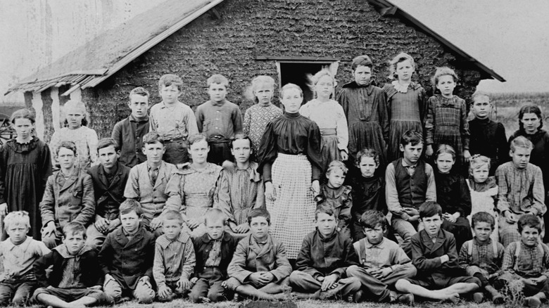 barn och vuxna framför litet hem i prärien på 1800-talet