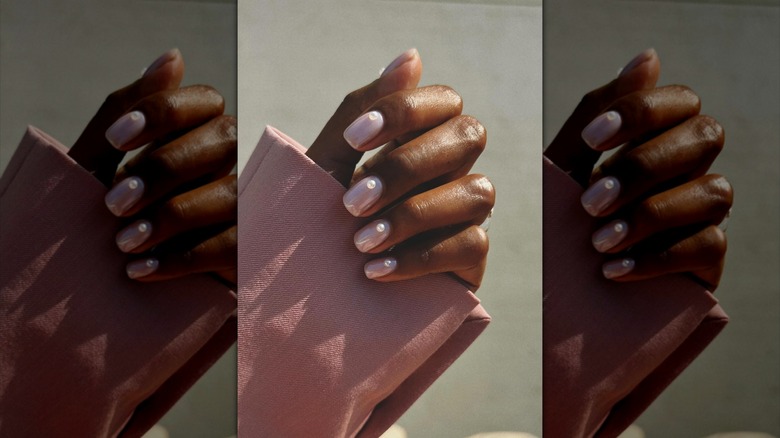 En hand som bär nakenrosa nagellack med pärla accenter.