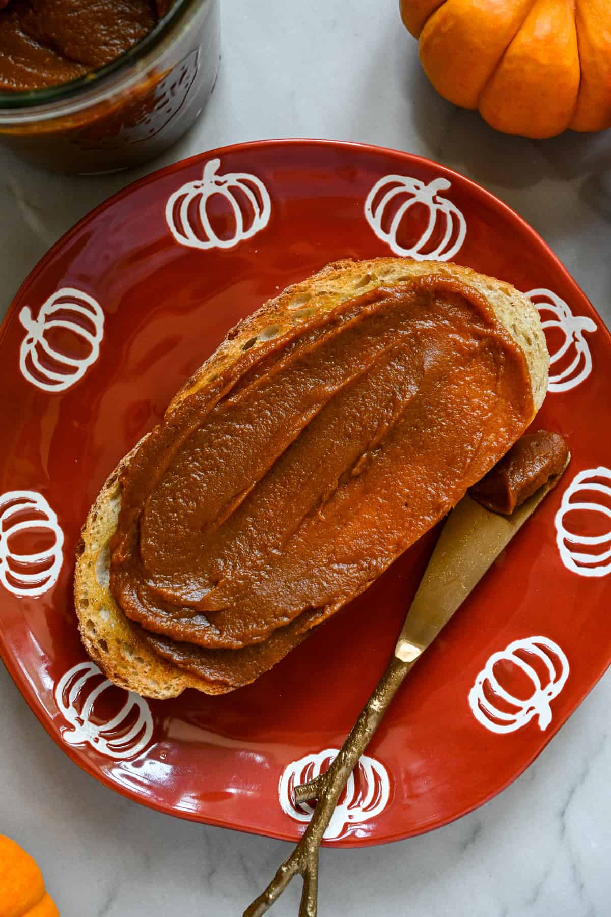 En skiva rostat bröd med hemgjort pumpasmör på en apelsin tallrik med pumpor runt kanten.