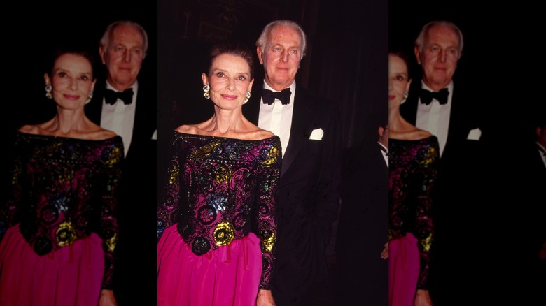 Audrey Hepburn i en omständligt mönstrad off-the-shoulder-klänning och den franske modedesignern Hubert de Givenchy i smoking på ett modeevenemang.