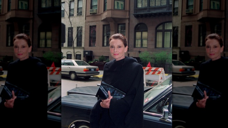 Audrey Hepburn på gatan i New York City på dagtid klädd i en svart kappa.