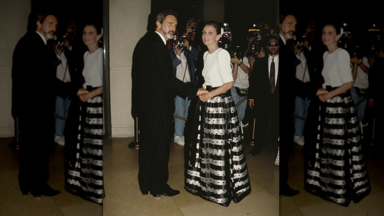 Audrey Hepburn på ett event klädd i en vit topp och svart-silverrandig hel kjol.