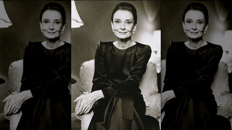 Audrey Hepburn poserar för ett porträtt iklädd en svart långärmad satinklänning.