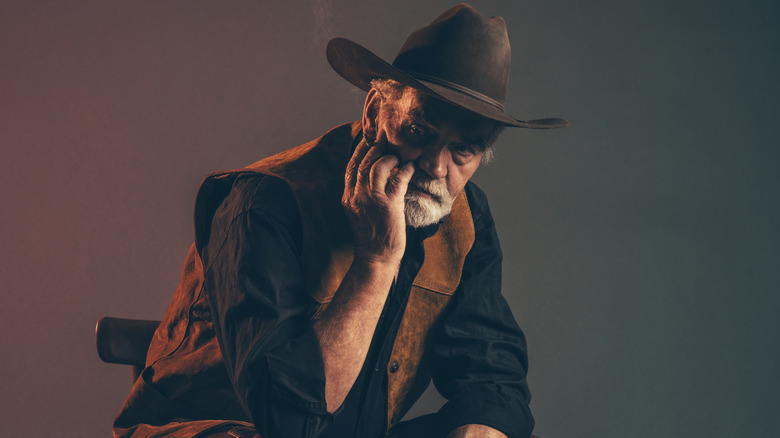 äldre cowboy ser sliten ut när han sitter på en liten stol