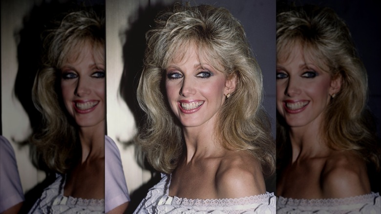 Morgan Fairchild 1984 leende i en off-the-shoulder klänning med fluffig lugg.