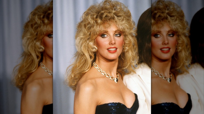 Morgan Fairchild 1982 vid en formell tillställning iklädd en glittrande klänning och halsband med voluminöst lockigt hår.
