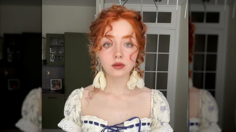 En rödhårig med cottagecore makeup och blomörhängen poserar för ett foto