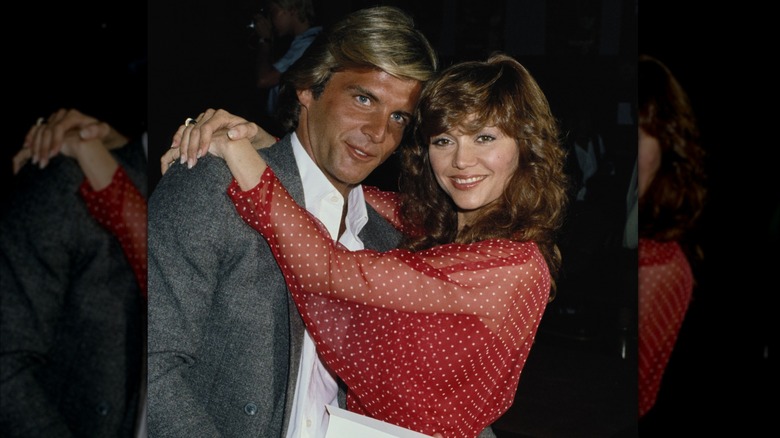 Victoria Principal klädd i en skir röd-vit prickig topp som kramar Christopher Skinner cirka 1979.
