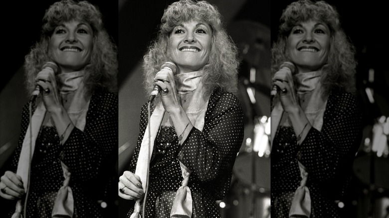 Stella Parton på bilden 1980 bär en halsduk och prickig klänning medan hon sjunger