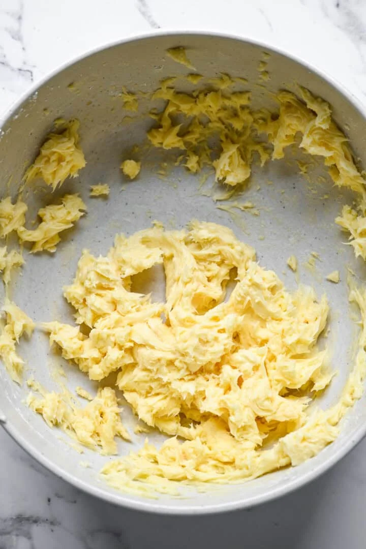 Blek, fluffig krämig smörblandning i en stor spräcklig mixerskål.