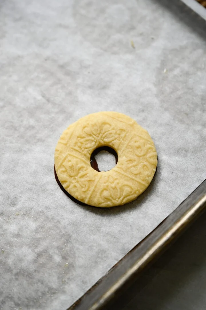 Präglad ringformad mördegskaka pressad ovanpå en ring av smält choklad på en bakplåtspappersklädd plåt.