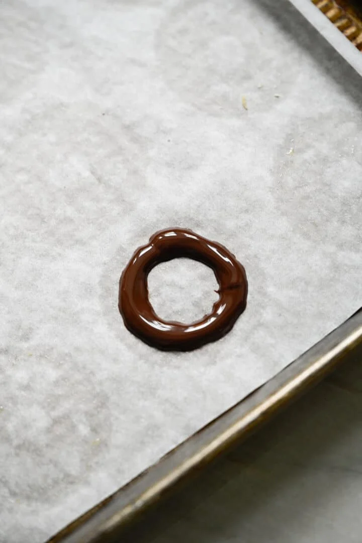 Ring av smält mörk choklad spridda på en bakplåtspappersklädd plåt.