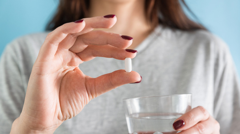kvinna som håller en statin i handen som hon ska ta med ett glas vatten