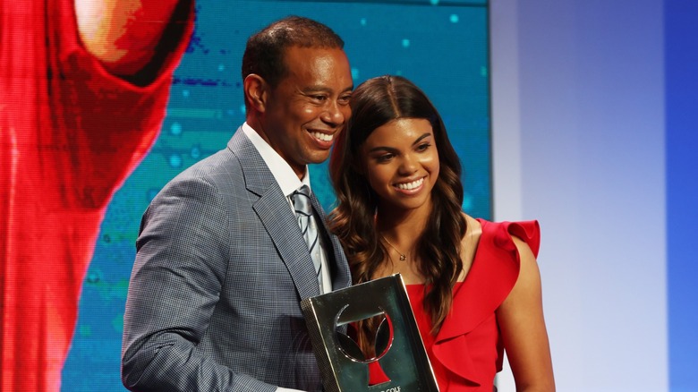Sam Woods poserar med sin far med håret nere i lösa vågor med en mittdel och en knallröd ärmlös klänning när hon deltar i World Golf Hall of Fame Induction Ceremony i Florida 2022.