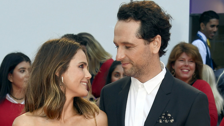 Keri Russell och Matthew Rhys ler medan de ger varandra tillgivna blickar på ett utomhusevenemang på röda mattan