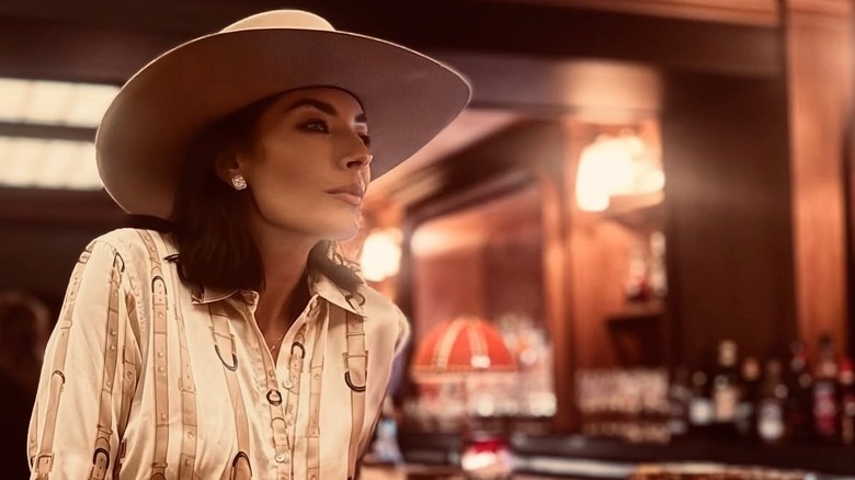 Nicole Sheridan sitter på en bar iklädd en skjorta i västerländsk stil och en cowboyhatt.