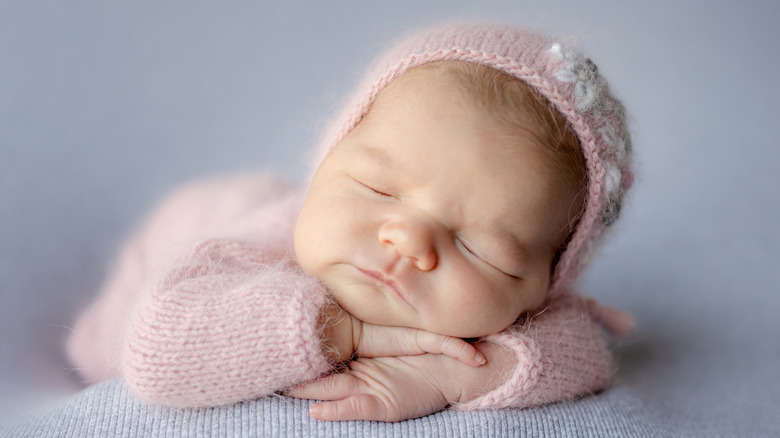 En nyfödd bebis sover i en rosa outfit och huva