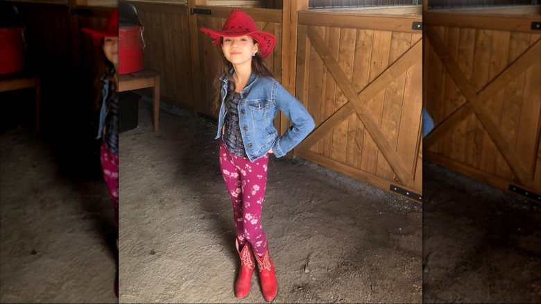 Skywalker Hughes ler i en röd cowgirlhatt och stövlar med leggings med prinka blommönster och en jeansjacka.