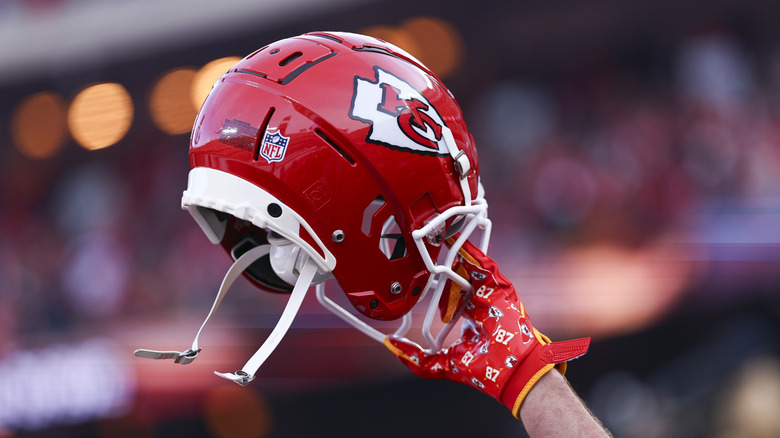Travis Kelces hand håller upp sin Kansas City Chiefs-hjälm under ett spel