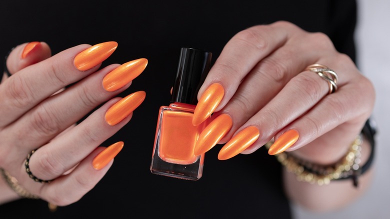 Händer med ljus orange manikyr som håller en flaska orange nagellack