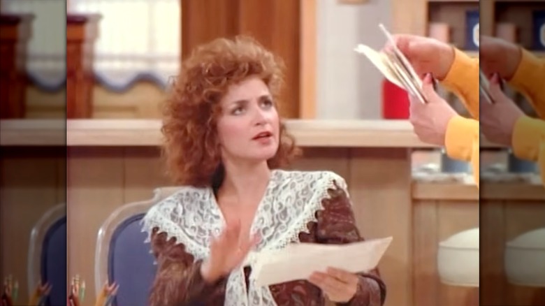 Annie Potts bär en brun spetsad blus med lockigt rött hår