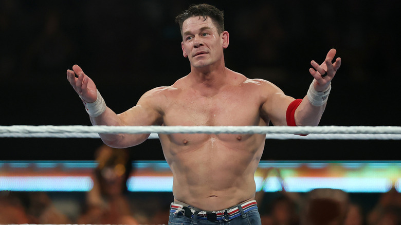 John Cena höjer båda händerna till publiken i en brottningsring under en match