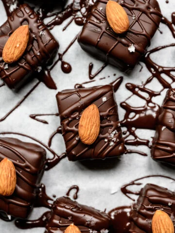 Närbild av chokladöverdragna barer toppade med hel mandel och flingsalt på pergament.