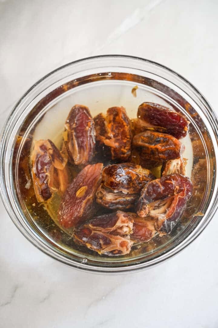 Ovanifrån av urkärnade, halverade dadlar som blötläggs i vatten i en glasskål.