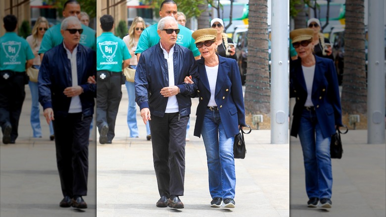 Judy Sheindlin går med sin man (L) iklädd utsvängda jeans och vit långärmad med blå kavaj och fiskarhatt