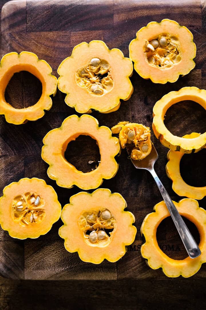 Ovanifrån av delicata squash rundor på en träskiva, fröna öste ut med en sked.
