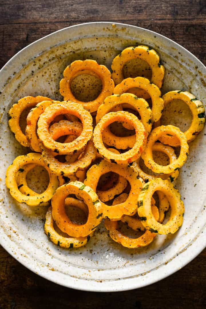 Ovanifrån av delicata squashringar kastade med olja och krydda i en vit skål.