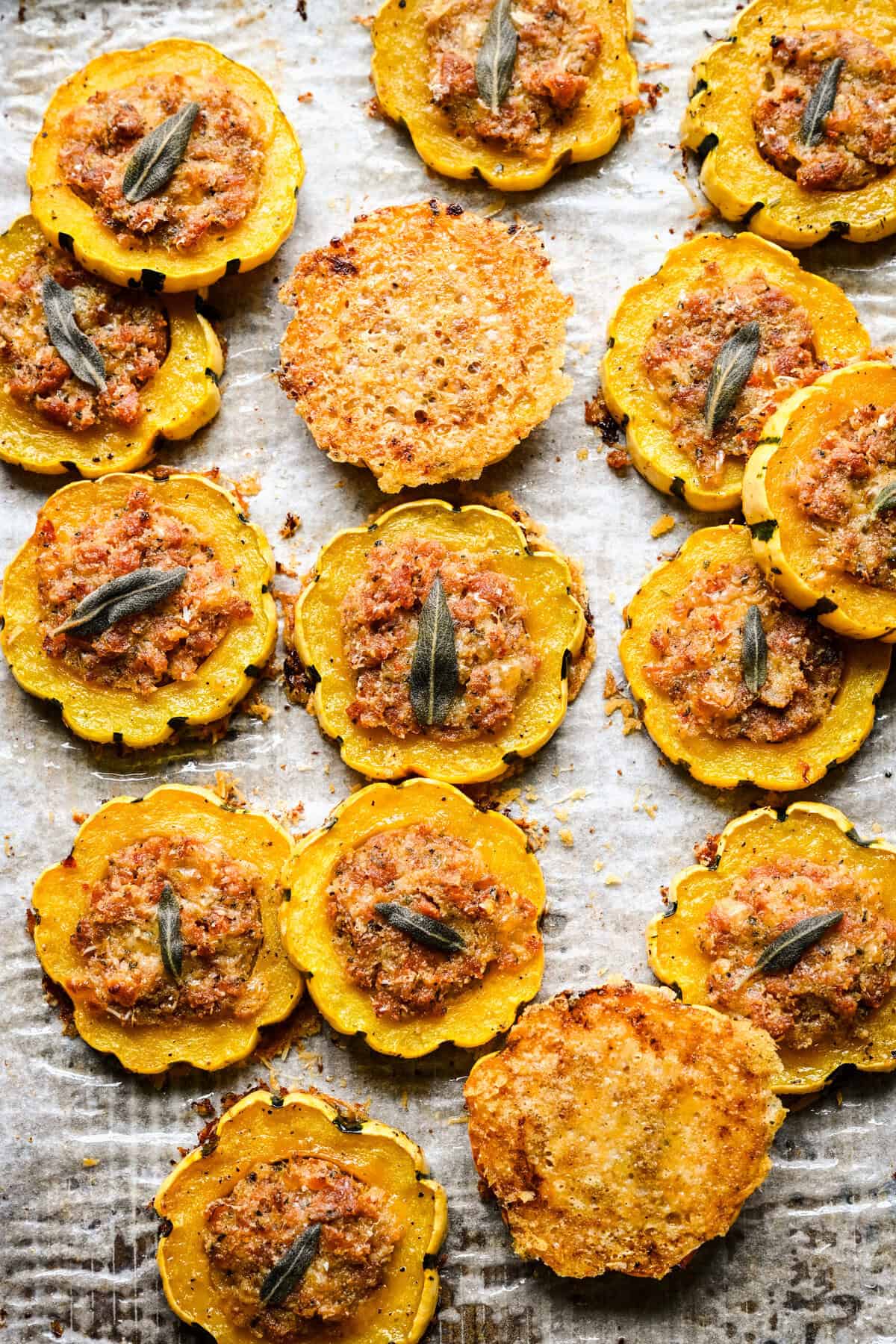 Ovanifrån av fyllda delicata squashringar och två parmesanchips på en bakplåtspappersklädd form.