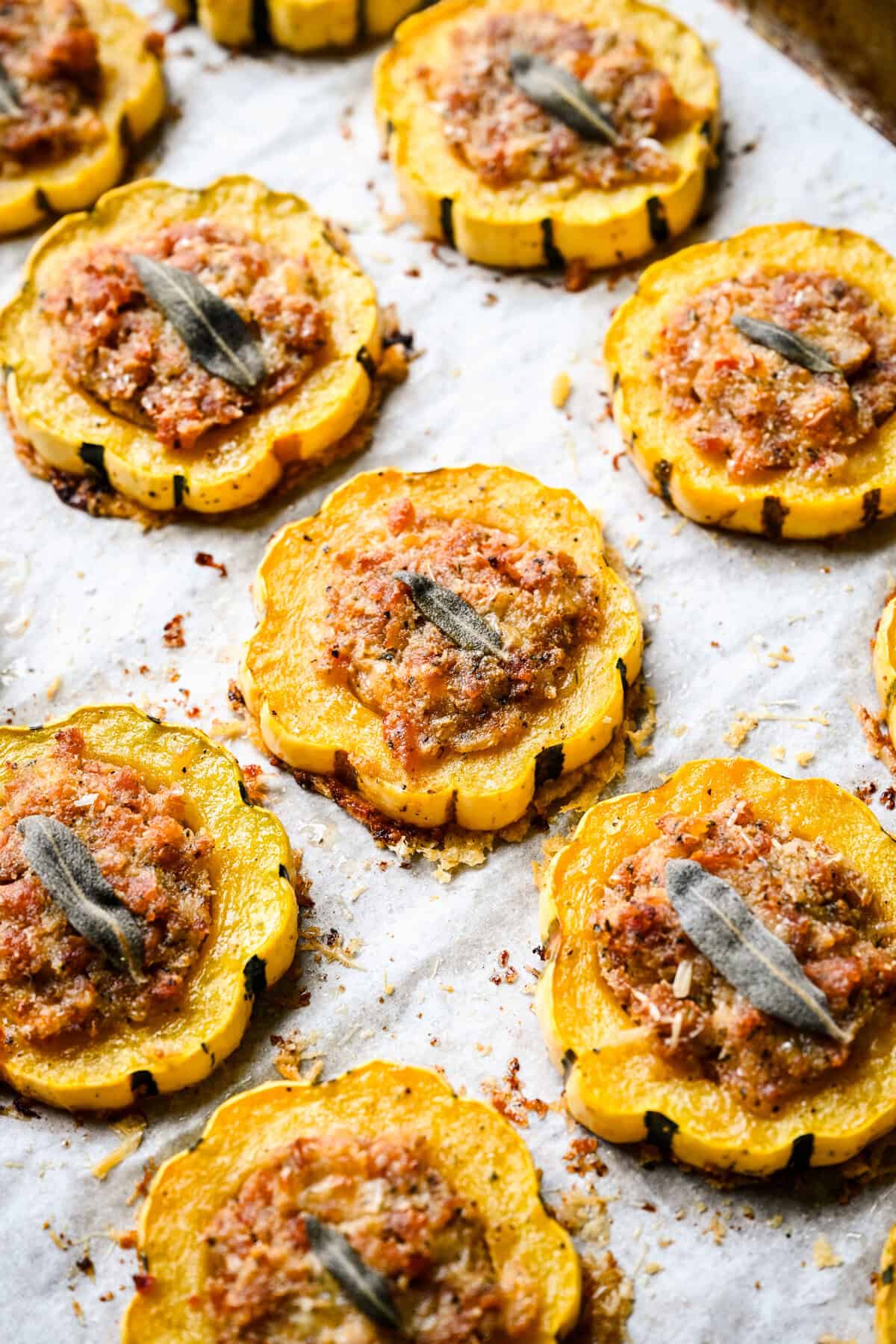 45 graders vy av bakad korv fyllda delicata squashringar på en bakplåtspappersklädd form.