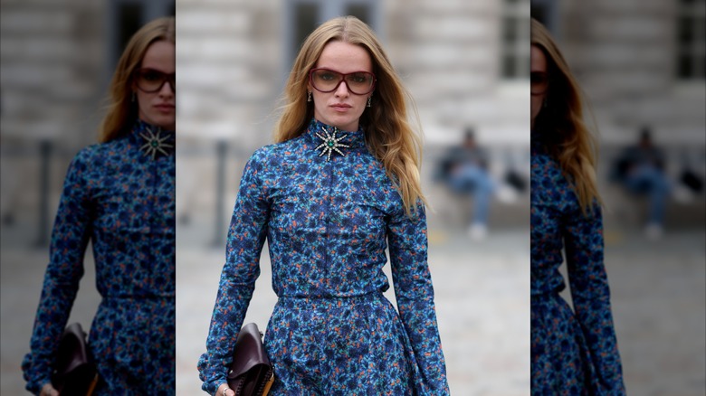 En blond tjej klädd i en blommig blå klänning och en utsmyckad brosch