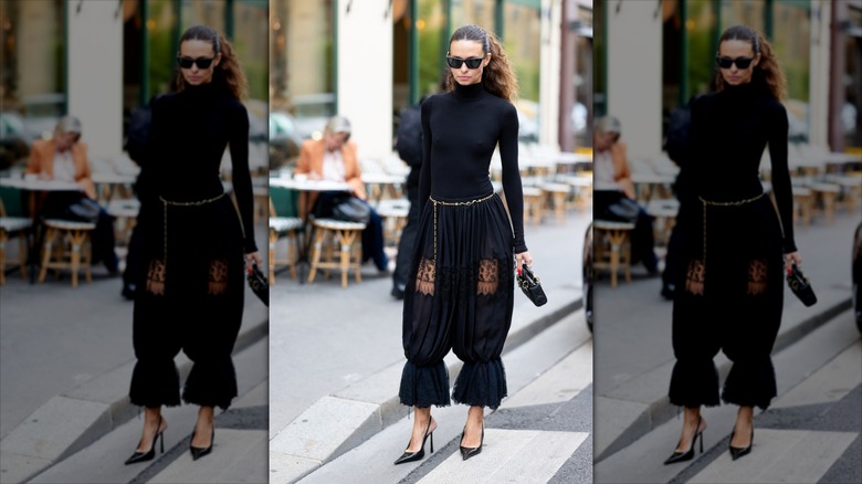 En brunettflicka som bär ett guldkedjebälte med svarta pantalons och en svart polotröja