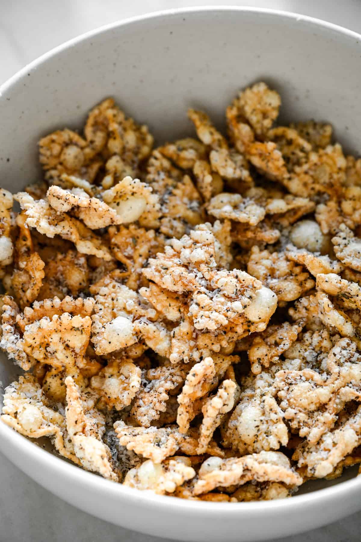 45 graders vy av kryddad puffad pasta som fyller en vit spräcklig skål.