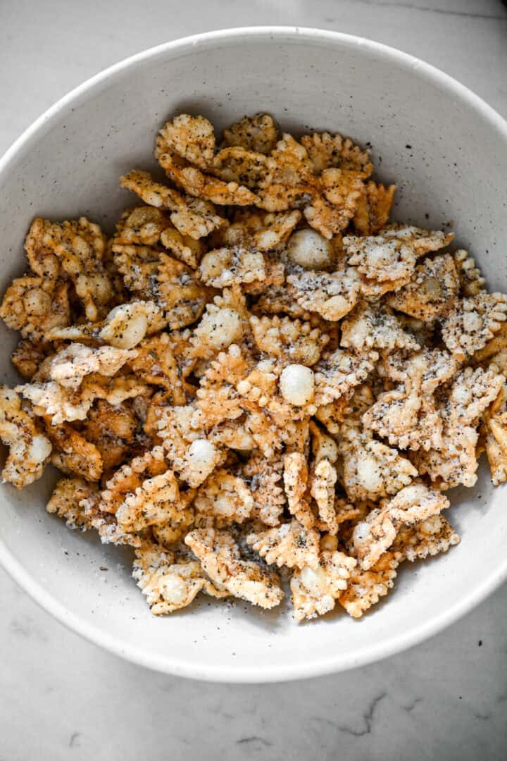 Ovanifrån av puffad pasta kastad med riven parmesan och svartpeppar i en vit skål.